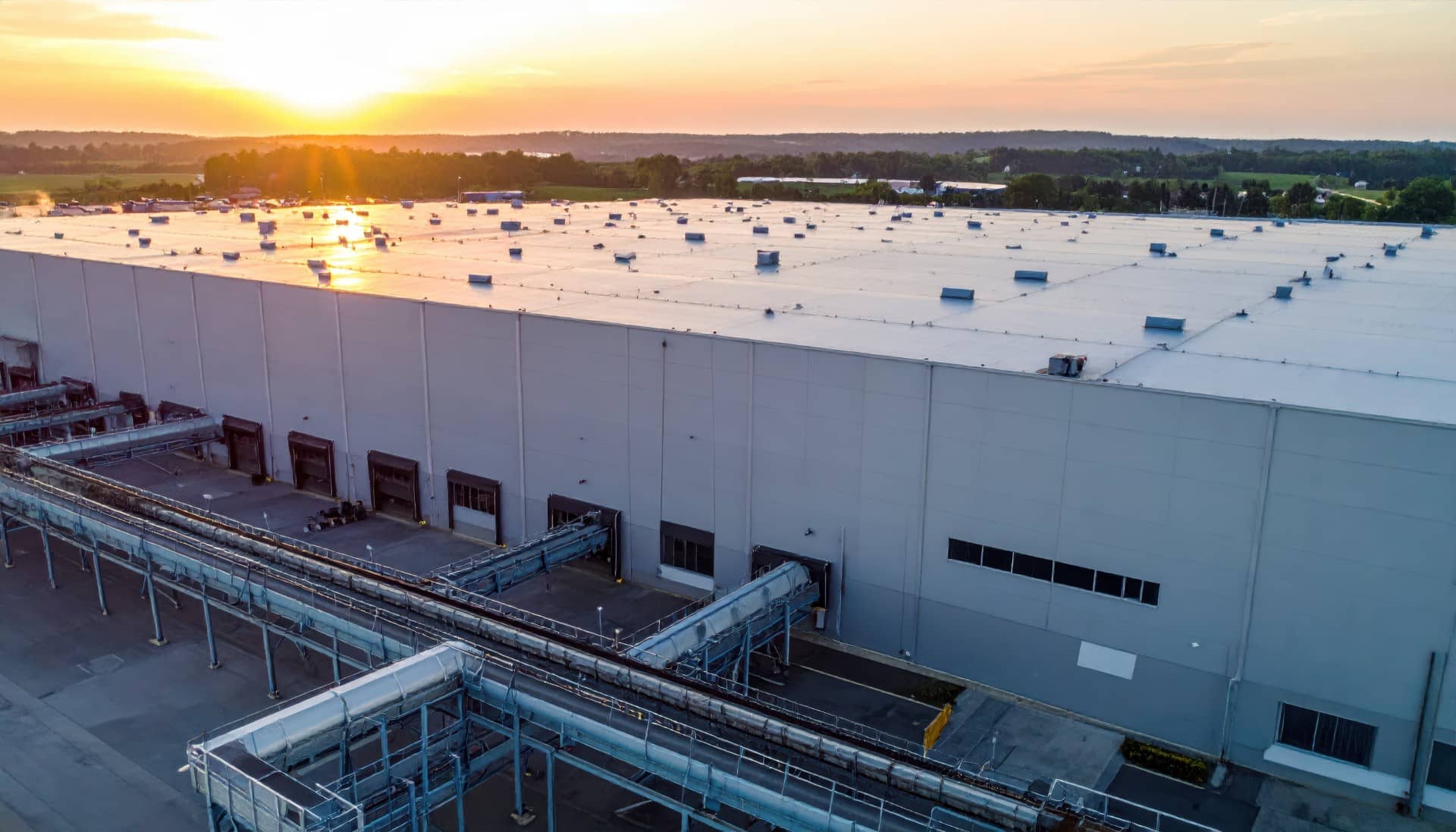Aerial view of a large commercial warehouse rooftop at sunset, demonstrating the scale of industrial cooling needs.